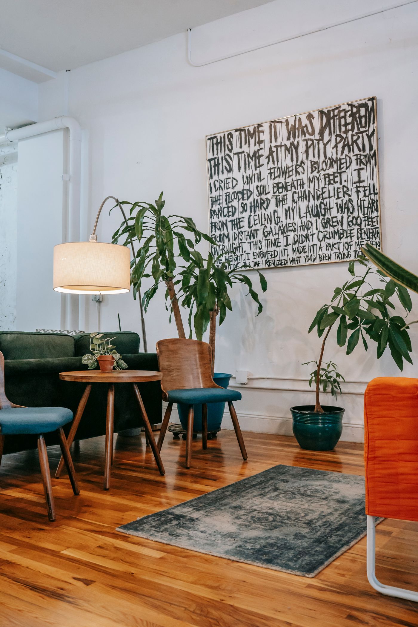 A light-filled sitting area with wood floors, green upholstery, and indoor plants